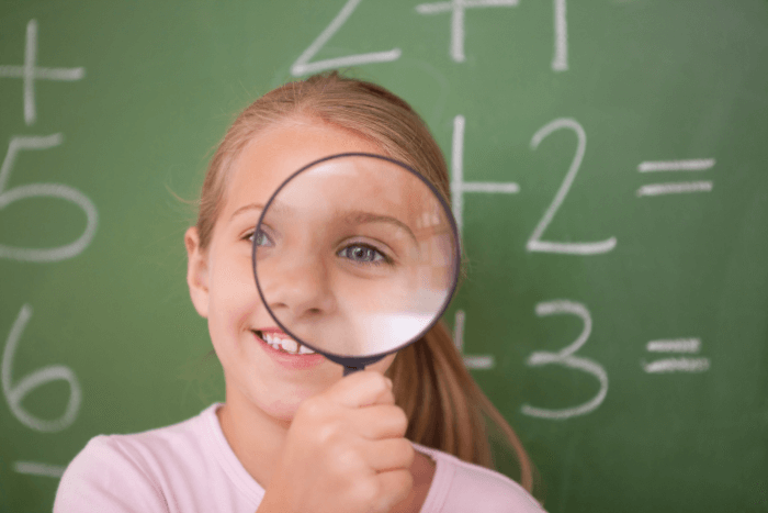 Buy a home in Pensacola – smiling young girl holding magnifying glass in front of school chalkboard