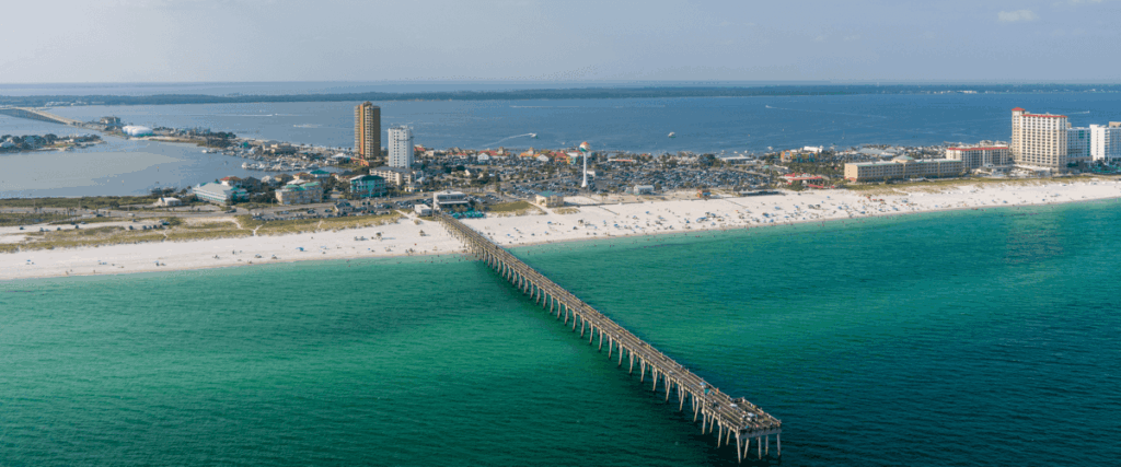 Aerial view of Pensacola Beach with a long pier extending into the Gulf of Mexico, ideal for those looking to buy a home in Pensacola.