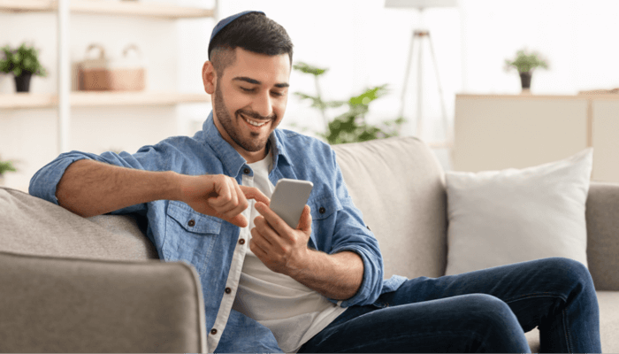 Smiling man sitting on a couch browsing his phone for listings to buy a home in Pensacola.
