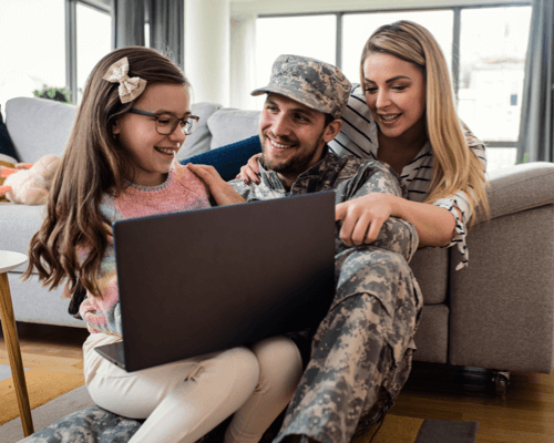Military family smiling together at home while browsing laptop, discussing how to buy a home in Pensacola.