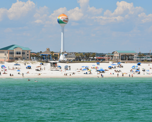 Beautiful sunny day at Pensacola Beach with people enjoying the white sand and emerald waters, highlighting the appeal to buy a home in Pensacola.