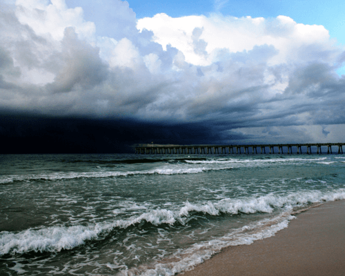 Storm clouds forming over the ocean near a pier in Pensacola, Florida, a reminder to consider weather when planning to buy a home in Pensacola.