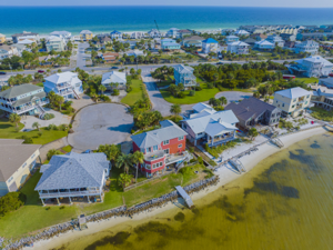 Aerial of a waterfront Pensacola neighborhood with colorful homes, private docks, and emerald shoreline—perfect to list your pensacola home.