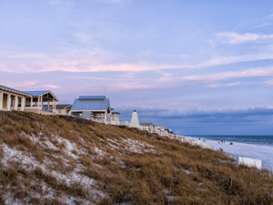 Row of Pensacola beach homes along sandy dunes at sunset with pastel skies.