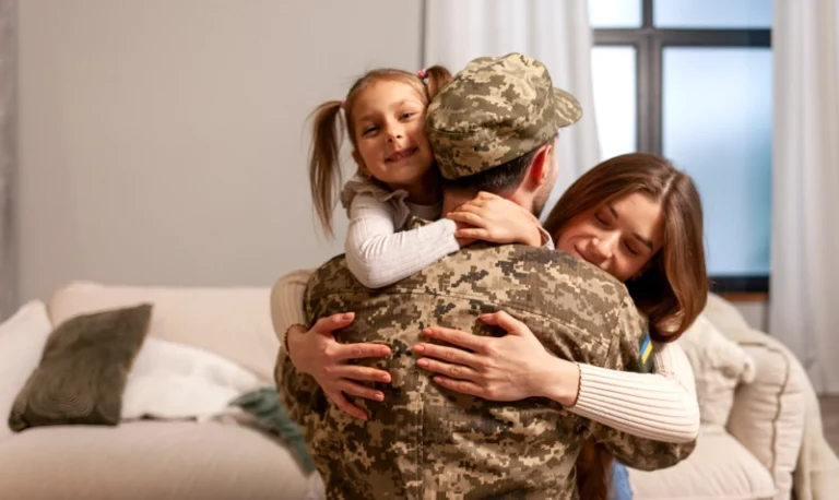 A uniformed military father hugging his smiling wife and daughter in a bright living room, illustrating the successful housing transition aided by a military relocation specialist.